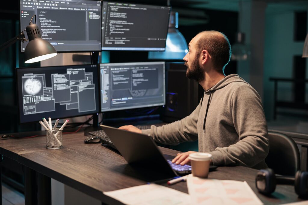 Software developer coding database on multiple monitors